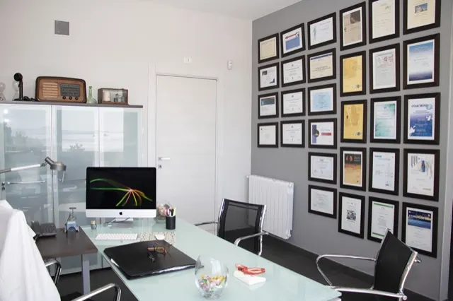 Lo studio con la scrivania in vetro e la parete di diplomi e attestati