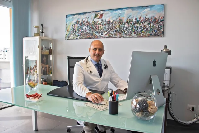 Il Dott. Russo alla scrivania dello studio, con il grande dipinto alla parete