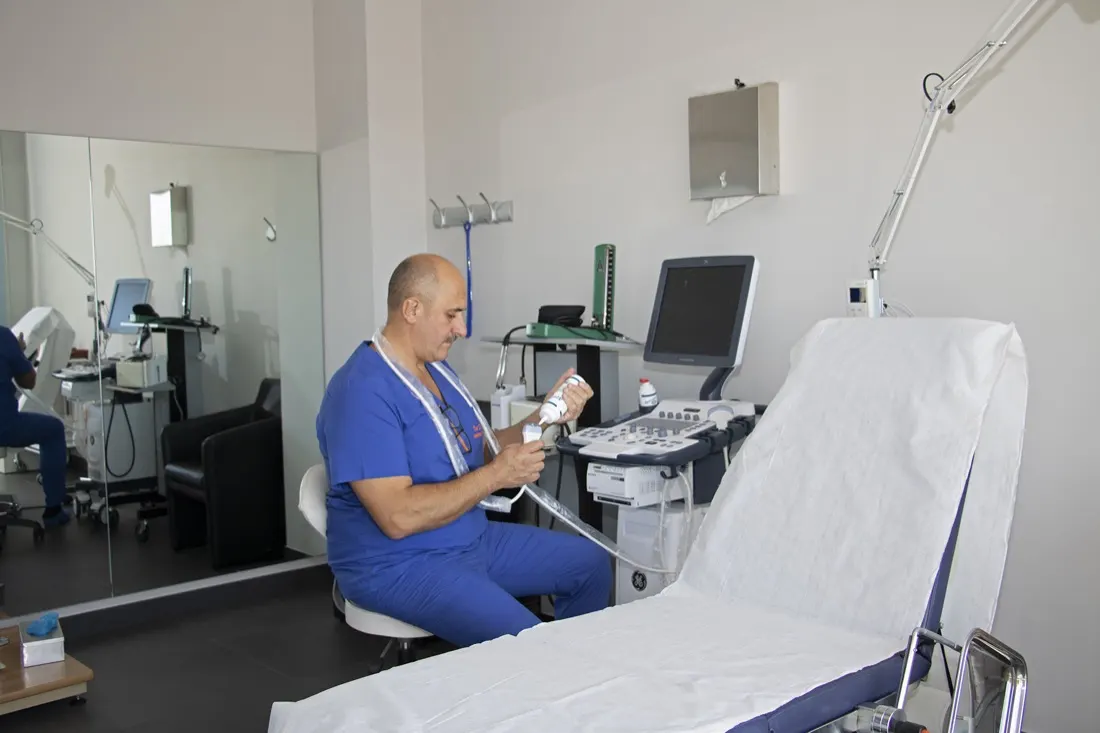 Il Dott. Russo in camice blu con la sonda dell'ecocolordoppler, seduto accanto al lettino